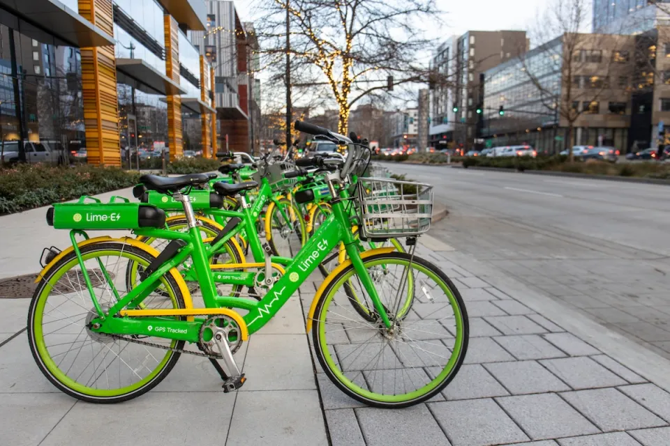 Row of green Lime electric bikes parked on sidewalk in Seattle with tree decorated with string lights in background.